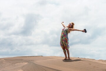 Fototapeta na wymiar Blonde smiling woman gesturing happiness on the top of a sand dune