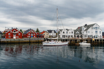 Fototapeta na wymiar Norwegian seascape, cityscape of the town Henningsvaer, a small boat moves between peninsulas, sail boat, rocky coast with dramatic skies, classic view of Norwegian houses on the slopes