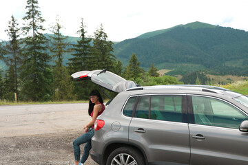 selective focus. Car on the side of the road. a young woman stands near a broken auto. Hitchhiking road trip concept. Mountain landscape. Road to the mountains. Part of a gray car. car rental. 