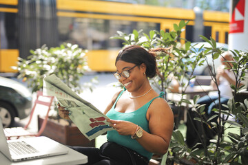 young woman reads a newspaper at the outside bar