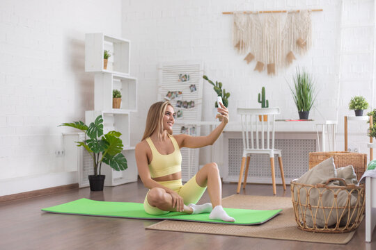 Woman taking a selfie while sitting on a yoga mat in the middle of the living room.