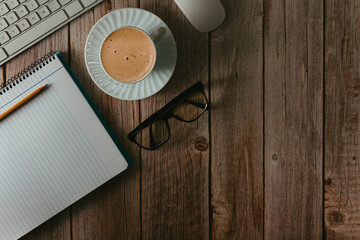 Workspace with computer keyboard, notebook, glasses and coffee cup on wooden background. Top view. Copy space. Selective focus.