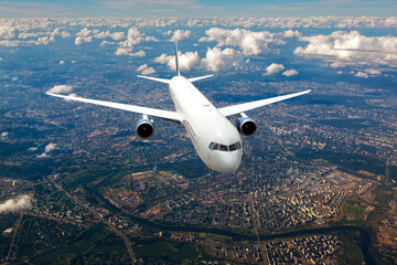 White passenger plane in flight. Aircraft  flies above the big city. Front view of aircraft.