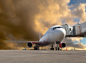 Fototapeta na wymiar Passenger plane at the airport runway. Airplane near the boarding bridge. Handling and preparing for the flight. Sunset clouds at background.