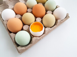 farm eggs are natural colored in an egg tray on a white background. one is broken