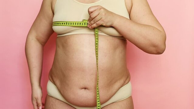 Cropped shot of adipose woman with big cellulite sagging tummy, measuring the circumference of her breast and chest with a tape roulette. Checking size after dieting. Showing off obesity problem body