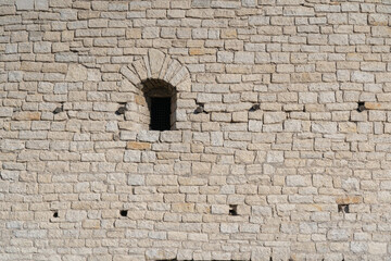 Fragment of the wall of the old fortress tower made of gray limestone. There is a vaulted loophole. Background. Texture.