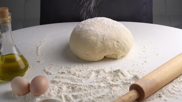 Male hands pour flour on dough and kneading dough. Closeup shot of chef making pizza dough on table