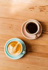 Two cups of coffee on a wooden flatlay background. Cappuccino on vegetable vegan milk in a blue cup and Americano in a pink cup top view