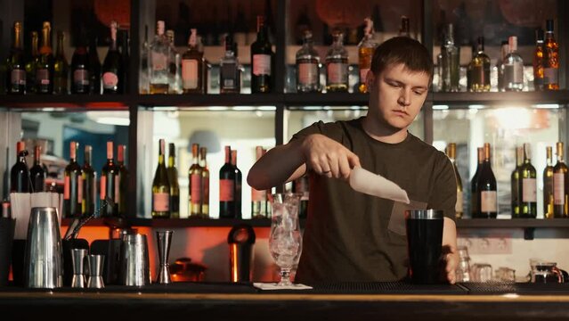 A professional bartender is preparing an alcoholic cocktail with ice cubes to customers at the bar or disco club,Sex on the beach cocktail.