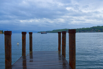 wooden jetty at a lake with ferry in the background in a cloudy day