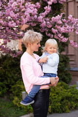 happy woman with little baby boy near pink sakura blooming tree. Spring concept