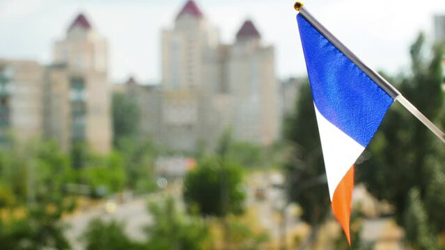 The national flag of France set against blue sky and city street. Tricolor French flag a vertical bands colored blue, white, and red flag. The holiday flag of the France waving. Copy space for text