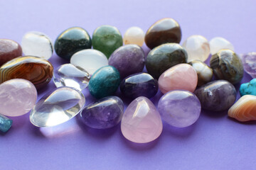 Tumbled gems of various colors. Amethyst, rose quartz, agate, apatite, aventurine, olivine, turquoise, aquamarine, rock crystal on purple background.
