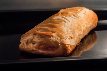 One baked puff pastry bun with apple jam on tray in electric oven - close up view. Homemade bakery, food, cooking and pastry concept