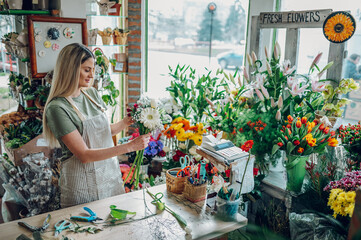 Female florist making a fresh flowers bouquet in a flower shop - obrazy, fototapety, plakaty