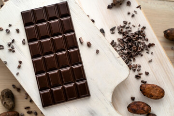 Dark bitter chocolate bar with cocoa beans on a wooden white background, top view. delicious chocolate. Space for text