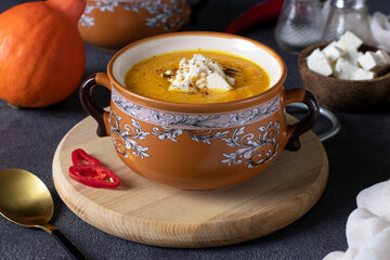 Pumpkin cream soup with feta cheese in brown bowl on wooden board. Closeup