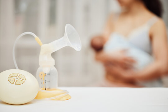 breast pump with breast milk against the background of a mother holding child.