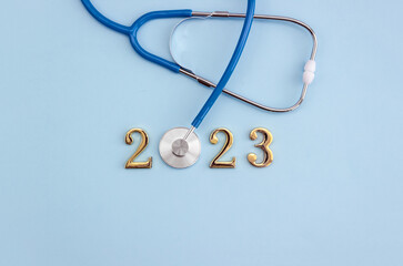 Stethoscope and gold numbers 2023 on blue background with copy space for your design. Happy New Year medical calendar cover