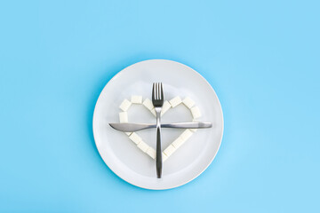Heart made of sugar cubes on plate and crossed fork and knife. Refusal of unhealthy food. The danger of obesity or diabetes. Sugarfree concept.