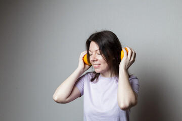 young attractive woman listens to music with headphones. Joking photo. Two halves of an orange...