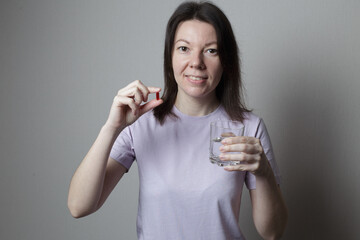 beautiful woman is taking a pill. woman in a pink t-shirt holding a glass of water and a pill