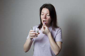 beautiful woman is taking a pill. woman in a pink t-shirt holding a glass of water and a pill