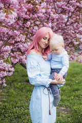 happy woman and little son in nature playing at spring park in the blooming Sakura gardens. Little boy and mother have a good time on weekend activity