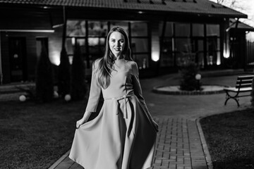 Naklejka premium A beautiful young woman in pink dress walks towards the camera, a beautiful building with night illumination. BW
