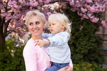 happy mother with little baby boy near pink sakura blooming tree. Spring concept