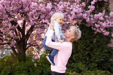 Obraz premium Little boy and mother have a good time on weekend activity in the blooming Sakura gardens. Mom and little son in nature playing at spring park.