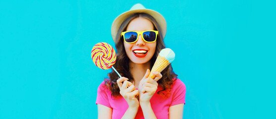 Portrait of happy laughing young woman with ice cream and lollipop wearing summer straw hat on blue...