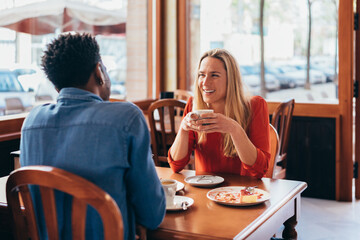 multiethnic couple converse while sitting at a bar table and drinking coffee