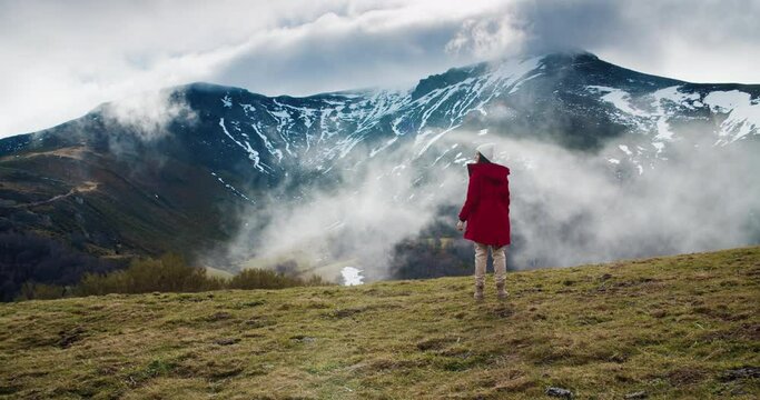 Traveler standing on top of mountain and expecting floating clouds. Solo hiker young adult woman take a break on her adventure. Concept of travel and discover on vacations