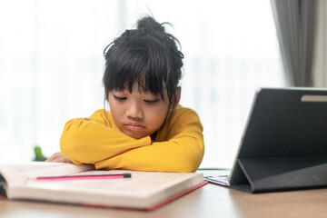 Little Asian girl sitting alone and looking out with a bored face, Preschool child laying head down on the table with sad  bored with homework, spoiled child