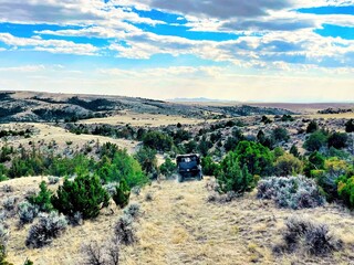 Under a partly cloudy sky on a summer day in the mountains of Montana, a four by four travels along a grassy hillside trail surrounded by rocks and shrubs.