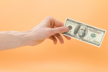 A man holds a american 100 dollars on an orange background. Rate. Trade. Economy. Pay. Payment. Rich. Business. Diplomacy. Buying. Change. Credit. Crisis