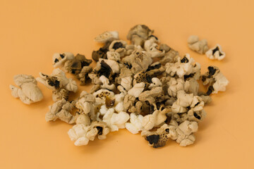 A heap of burnt popcorn lays on a yellow background. Dirty. Flake. Forget. Treat. Nourishment. Lose. Miss. Fail. Collapse. Crash. Waste. Eating