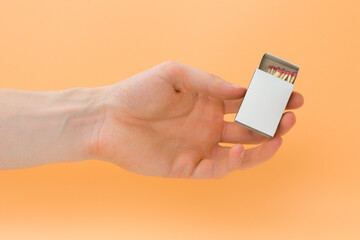 A man holds a white empty matchbox on a yellow background. Person. Caution. Package. Offensive....