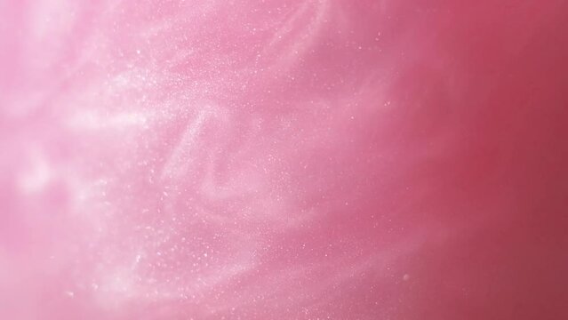 Glittering abstract pink background. Color fluid is swirling in beautiful silver clouds. Glitter dust is moving slowly in water. Amazing abstract texture background.