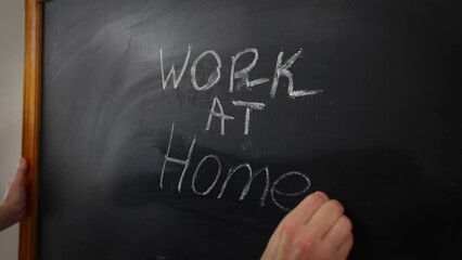Close-up blackboard with female hand writing Work at home announcement with chalk. Unrecognizable Caucasian woman indoors in office on coronavirus pandemic quarantine. New normal on lockdown