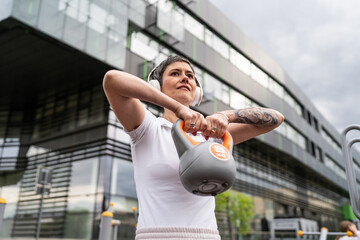 One woman modern mature caucasian female with short hair training in front of building in day with kettlebell weight at outdoor gym Sport fitness healthy lifestyle concept copy space