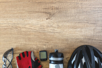 Bicycle accessories in a row black helmet, water bottle, goggles, bike computer and red gloves on a brown wooden background. Sport lifestyle concept with place for text