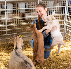 Portrait of positive woman farmer working in barn feeding goatlings and having fun