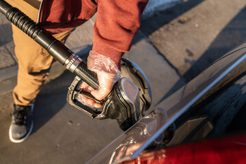 Close up on hand of unknown caucasian man hold black gas pump nozzle pouring gasoline into the fuel...