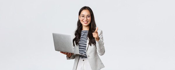 Fototapeta Business, finance and employment, female successful entrepreneurs concept. Smiling pleased businesswoman praise coworker who made good point, pointing finger camera satisfied, hold laptop obraz