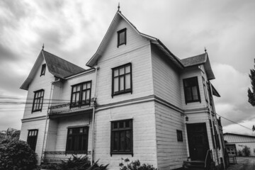 Three story old centuries white wood house with a lot windows in a cloudy day, Valdivia, Chile (in black and white)