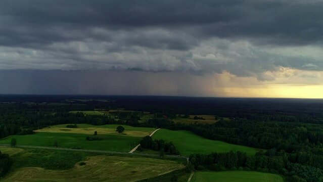 Aerial drone shot of rainfall in the background over scenic farmland and road with cars passing by in the rural countryside. Dark clouds.