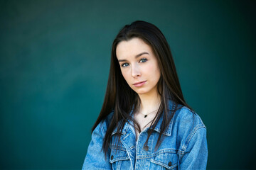 Fototapeta premium A beautiful teen brunette girl with a serious look leaning against a wall in thought with a teal green turquoise background